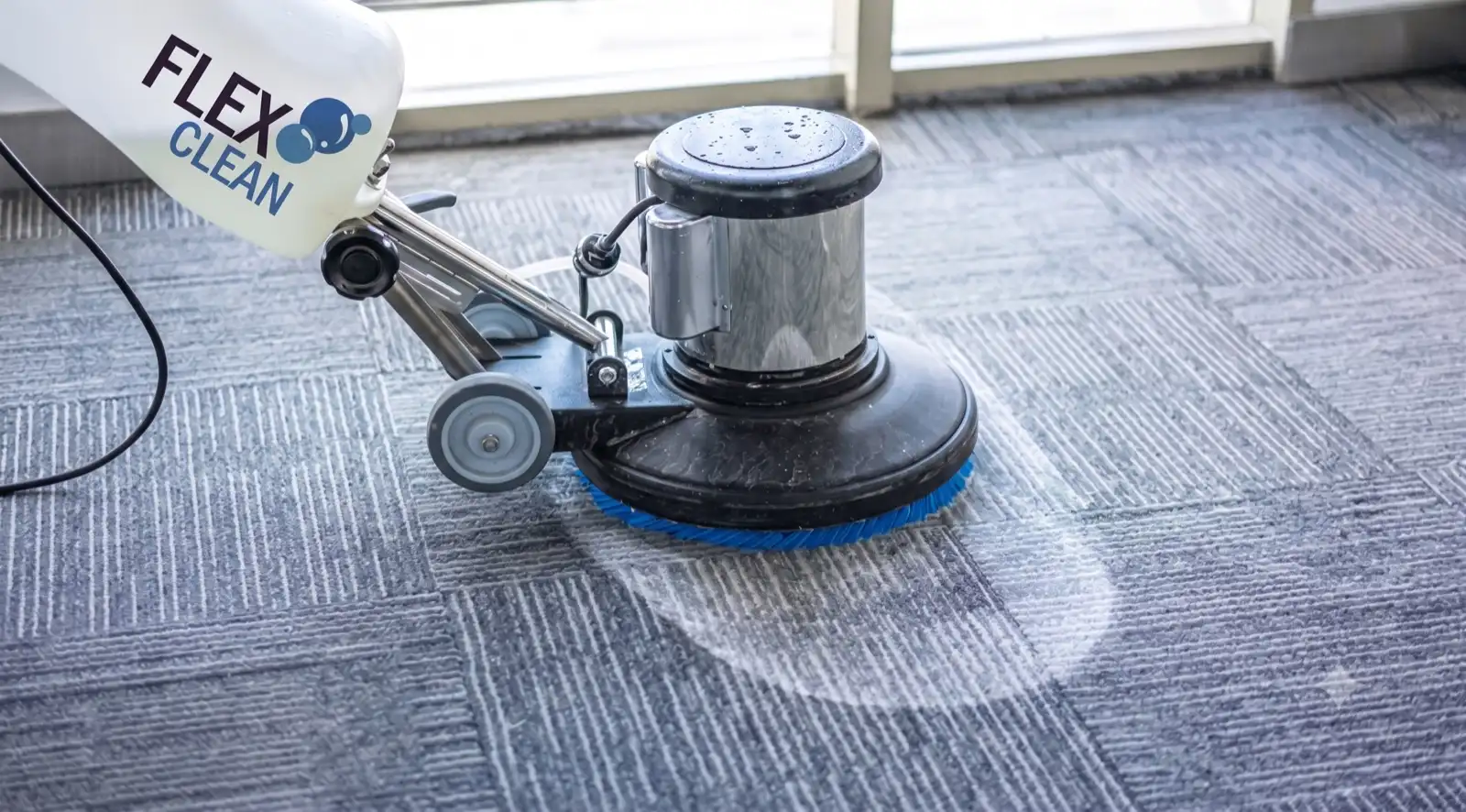 Máquina rotativa da Flex Clean com escova azul higienizando carpete cinza e revelando a área limpa